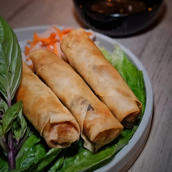 Three crispy Vietnamese spring rolls on a bed of lettuce with pickled carrots and basil.